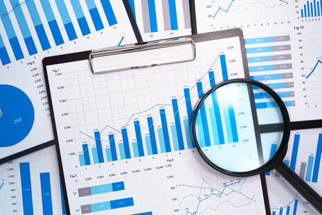 Draufblick auf einen Schreibtisch mit zahlreichen Unterlagen mit statistischen Auswertungen, Balken- und Säulendiagrammen